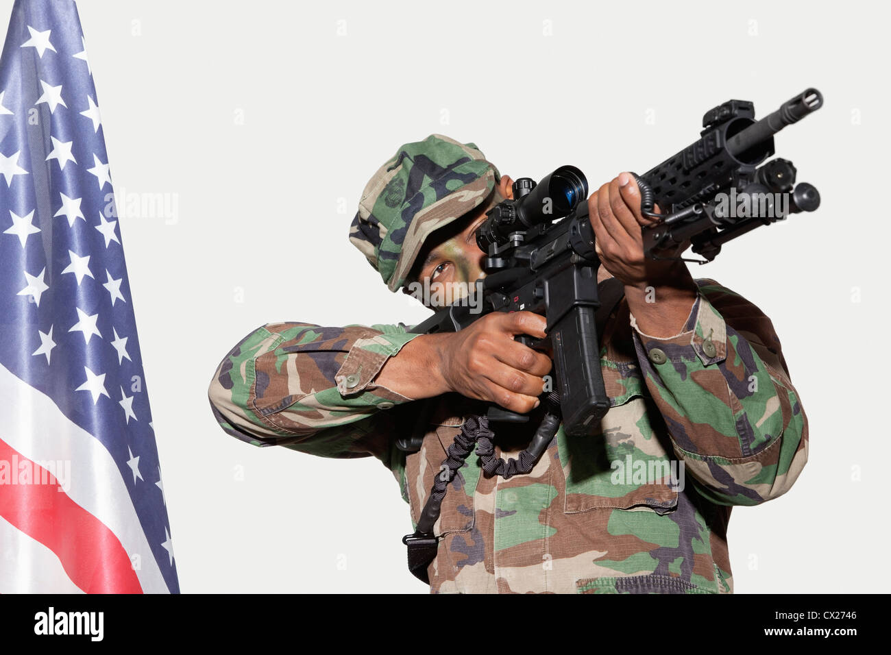 US Marine Corps soldier aiming M4 assault rifle with American flag against gray background Stock Photo