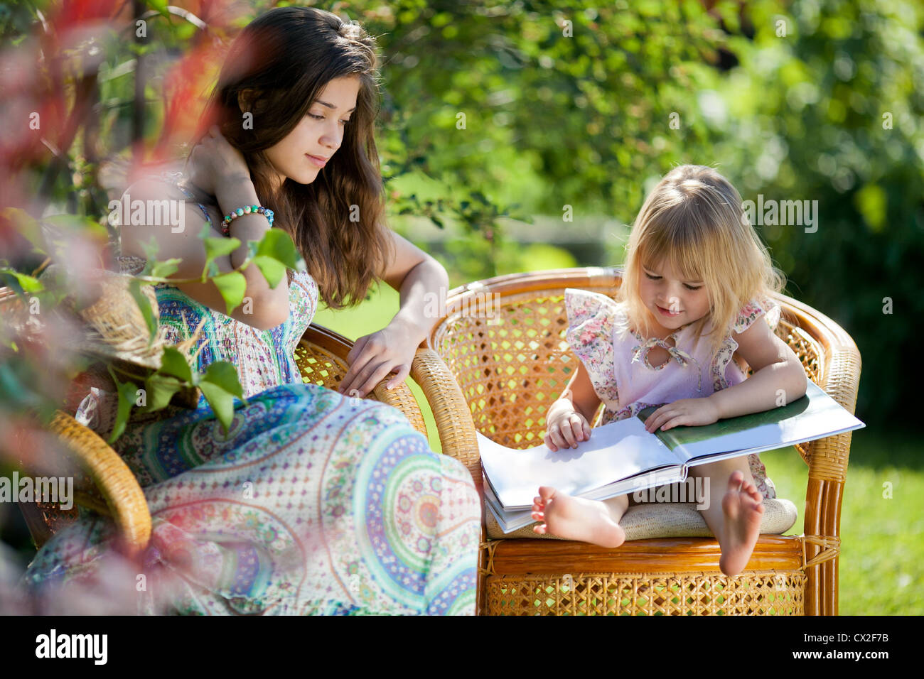 Girls reading book sitting in wicker chairs outdoor in summer day Stock Photo