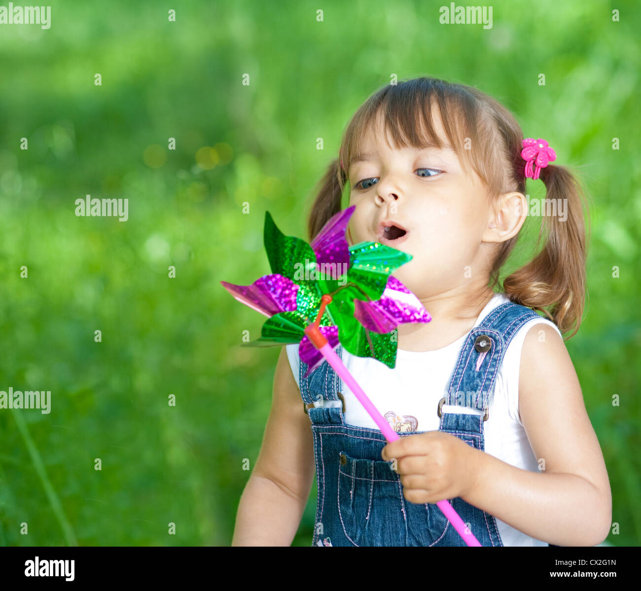 Little girl in jeans blowing on color propeller outdoor Stock Photo