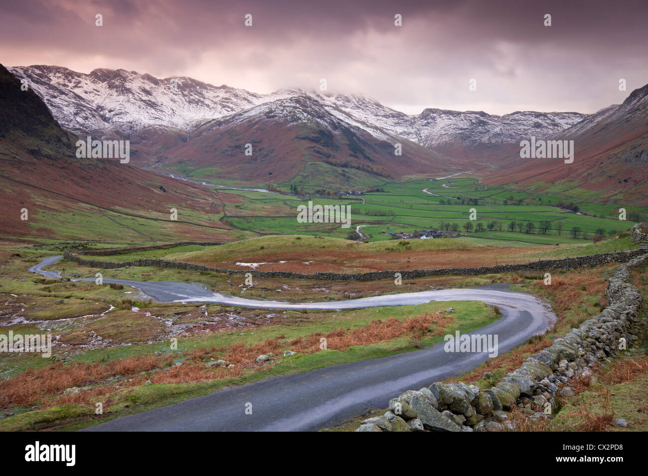 Small winding road leading into the Langdale Valley, surrounded by snow clad mountains, Lake District Stock Photo
