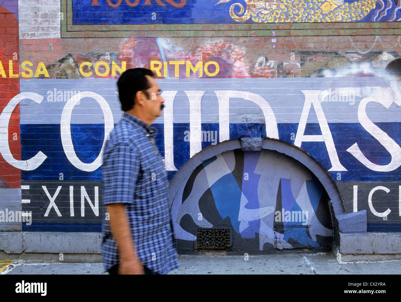 New York City East Spanish Harlem Street art.  The Barrio man walking in front of American graffiti wall painting. Public artworks USA Stock Photo