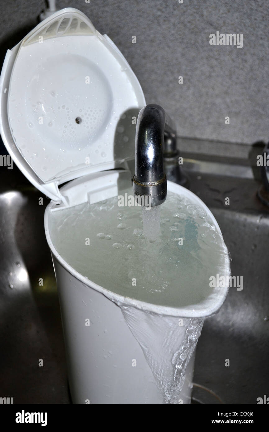 overflowing with water kettle / jug under tap / faucet Stock Photo