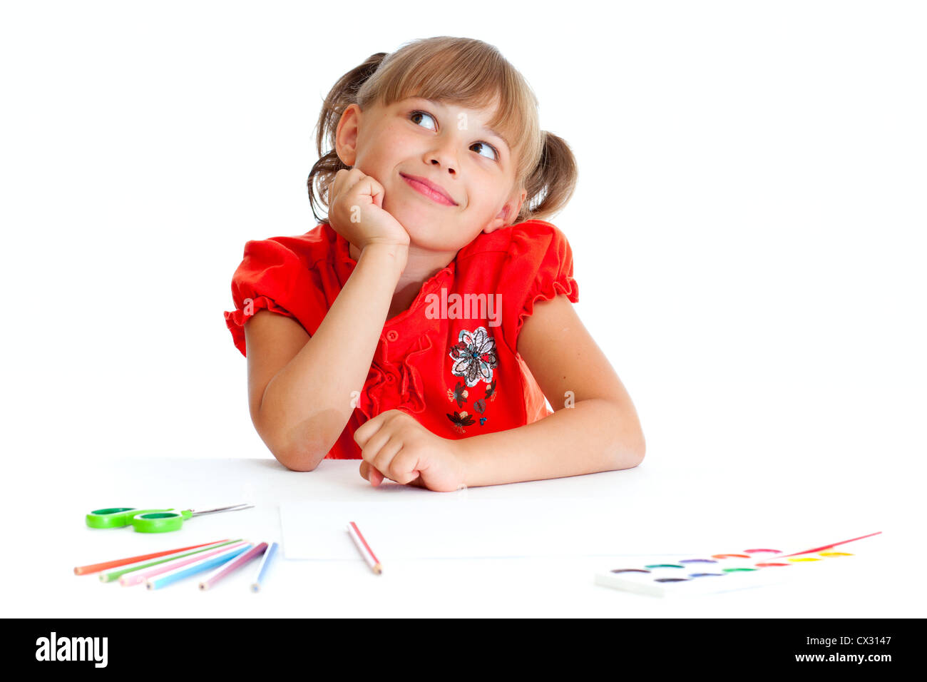 Schoolgirl is sitting at table with pencils, paints and scissors isolated Stock Photo