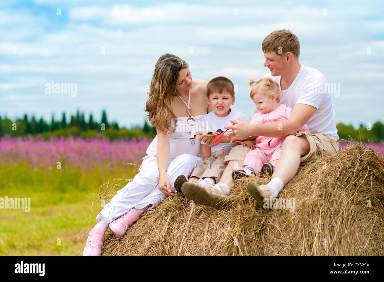 Happy family launching toy aircraft model sitting on haystack together Stock Photo