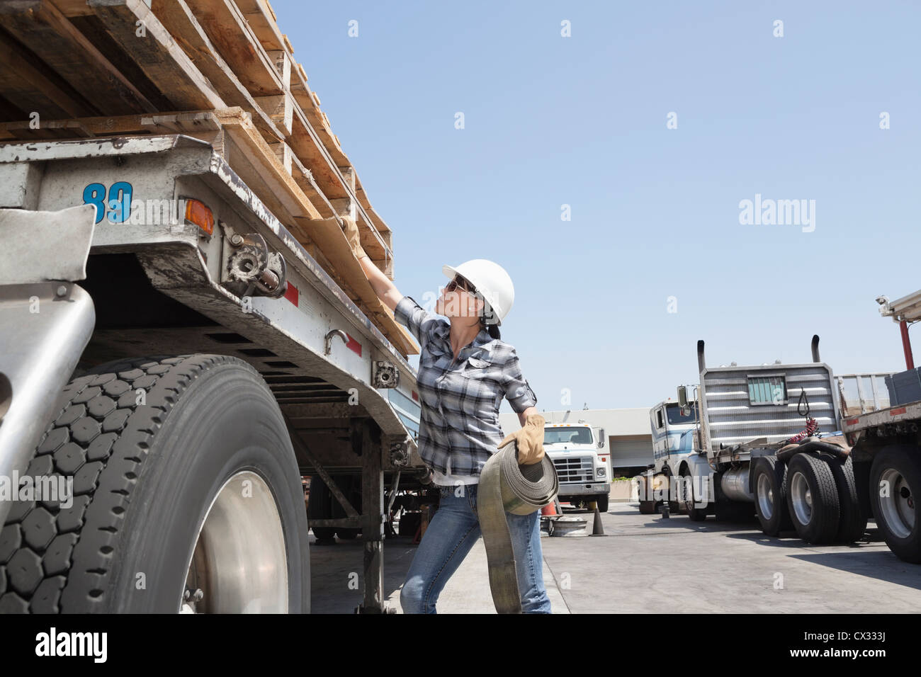 Female industrial worker strapping down wooden planks on logging truck