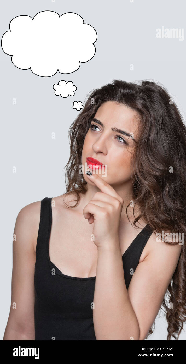 Thoughtful young woman with thought bubble looking away with hand on chin over gray background Stock Photo
