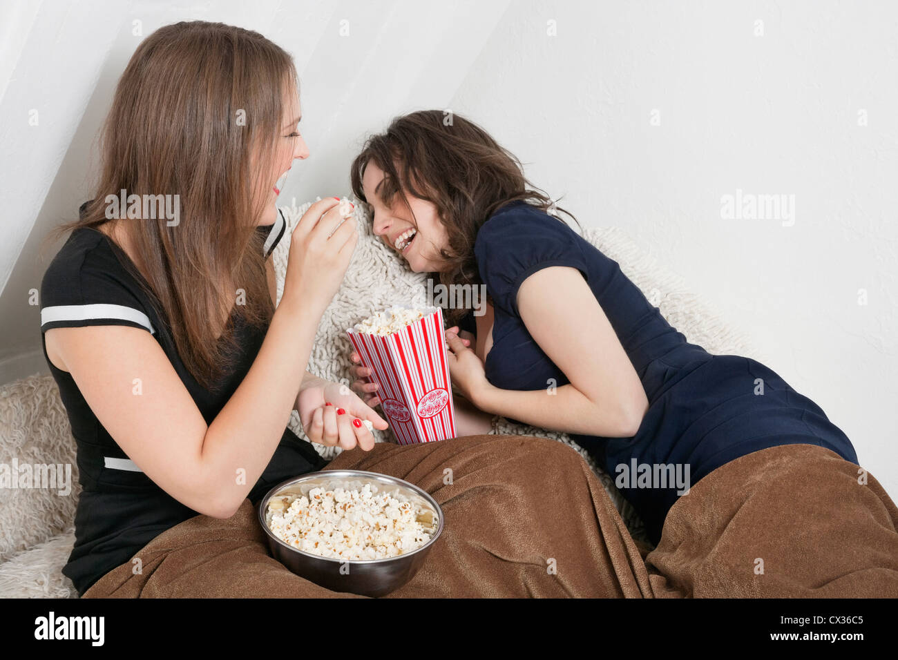 Cheerful young women eating popcorn in bed Stock Photo Alamy