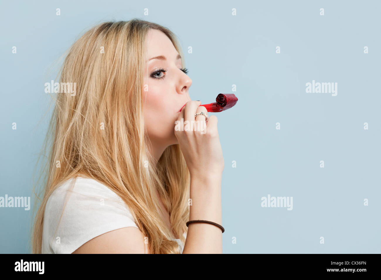 Young woman with party blower against light blue background Stock Photo ...