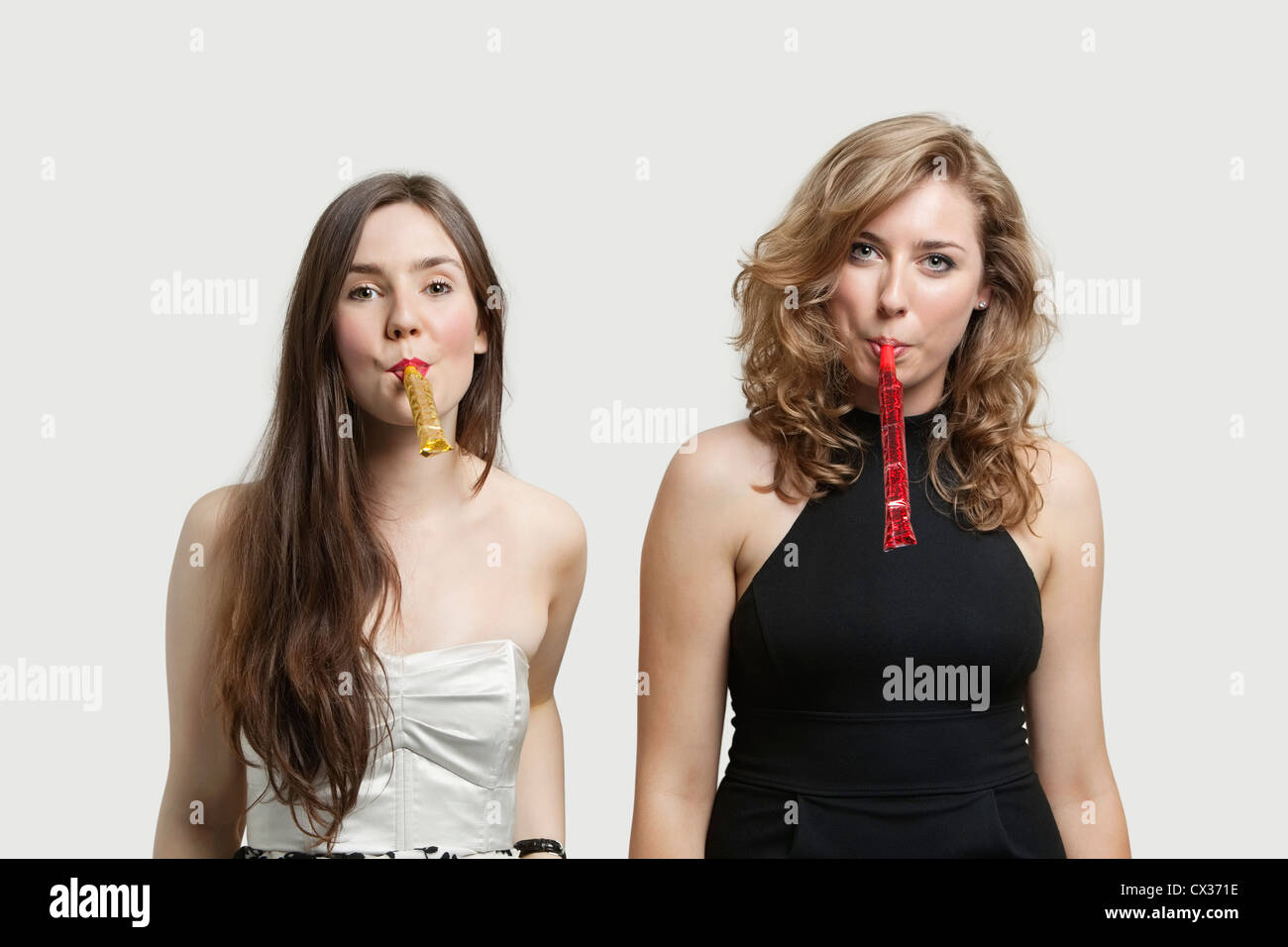 Portrait of young women blowing party puffers against gray background Stock Photo