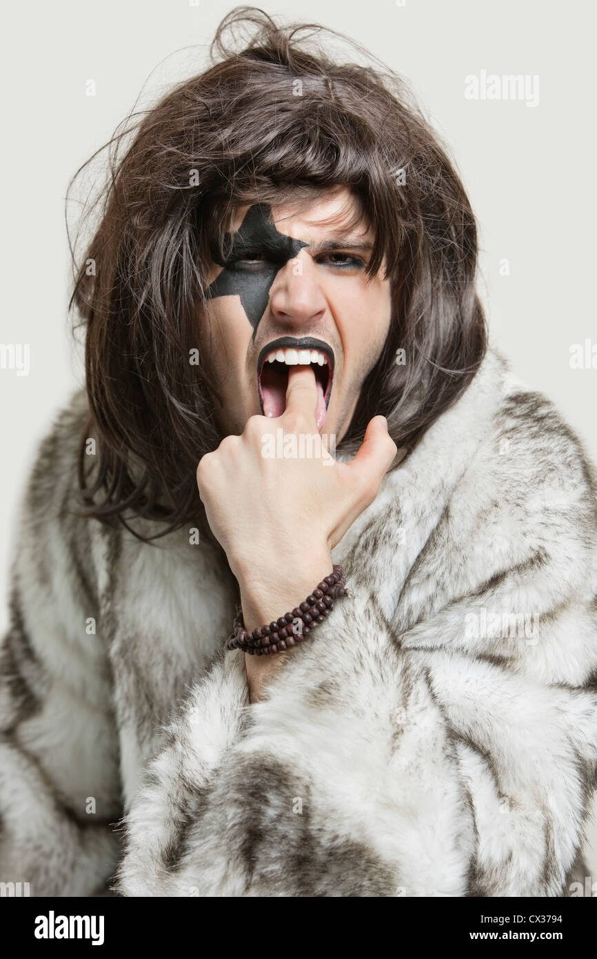 Portrait of young man in fur coat with finger in mouth against gray background Stock Photo