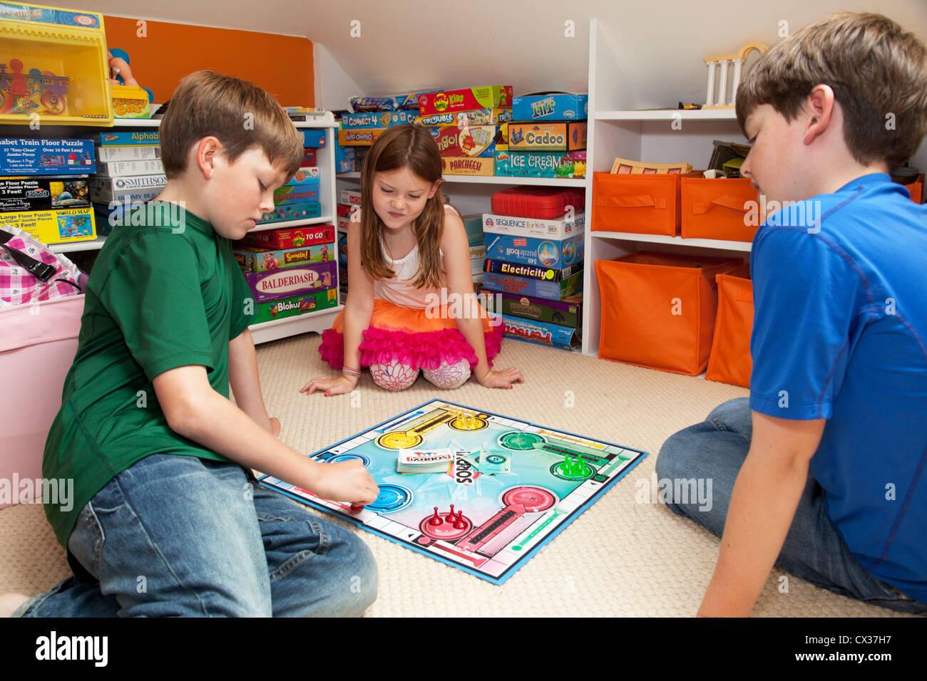 Three siblings are in their playroom playing a board game. Stock Photo