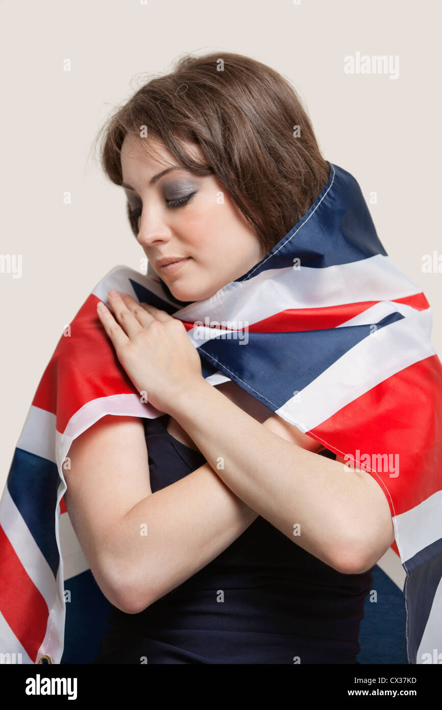 Young woman wrapped in British Flag over gray background Stock Photo