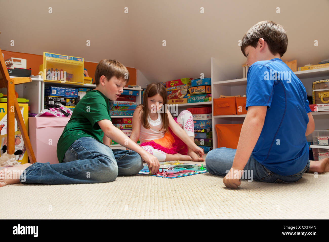 Three siblings are in their playroom playing a board game Stock Photo