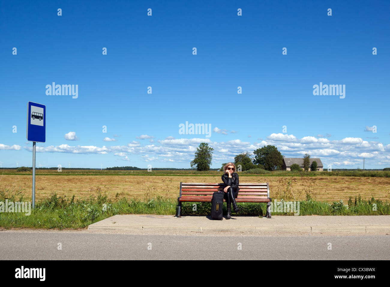 lonely woman sitting on a bench at a bus stop in the countryside Stock Photo