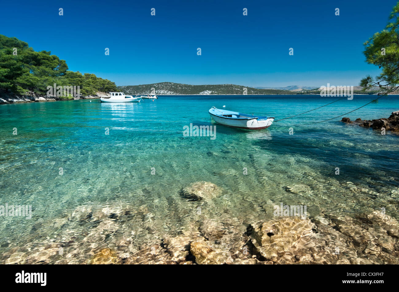 Transparent water with a boat and mountains in background. Bilo, Dalmatia, Croatia Stock Photo
