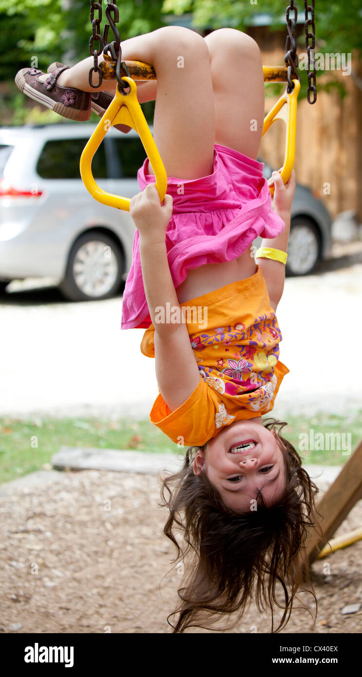 Little girl upside down hanging from trapeze monkey bars. Stock Photo
