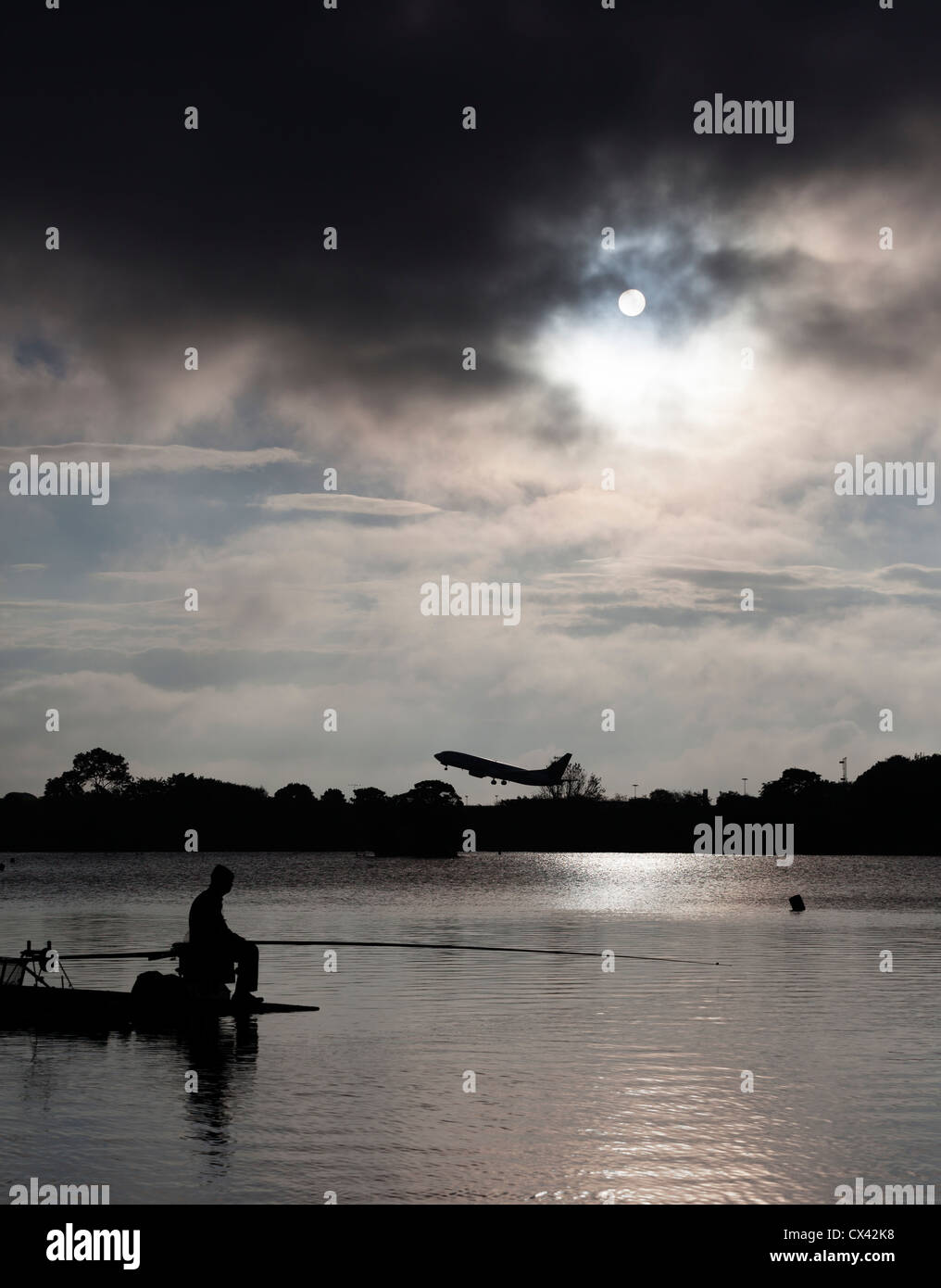 Man fishing in Yeadon Tarn as an aircraft takes off from Leeds Bradford Airport. Stock Photo