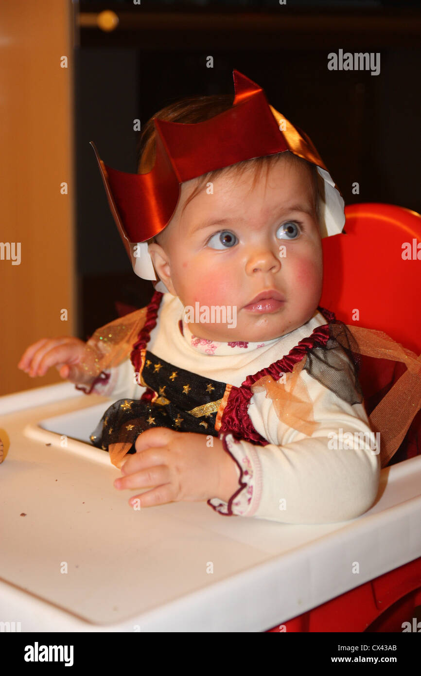 Little lovely beautiful baby girl in a high chair in a party crown hat and Christmas outfit Stock Photo