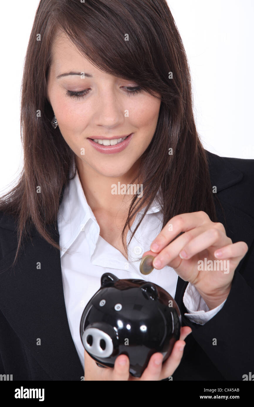 Young woman putting money into a piggy bank Stock Photo - Alamy
