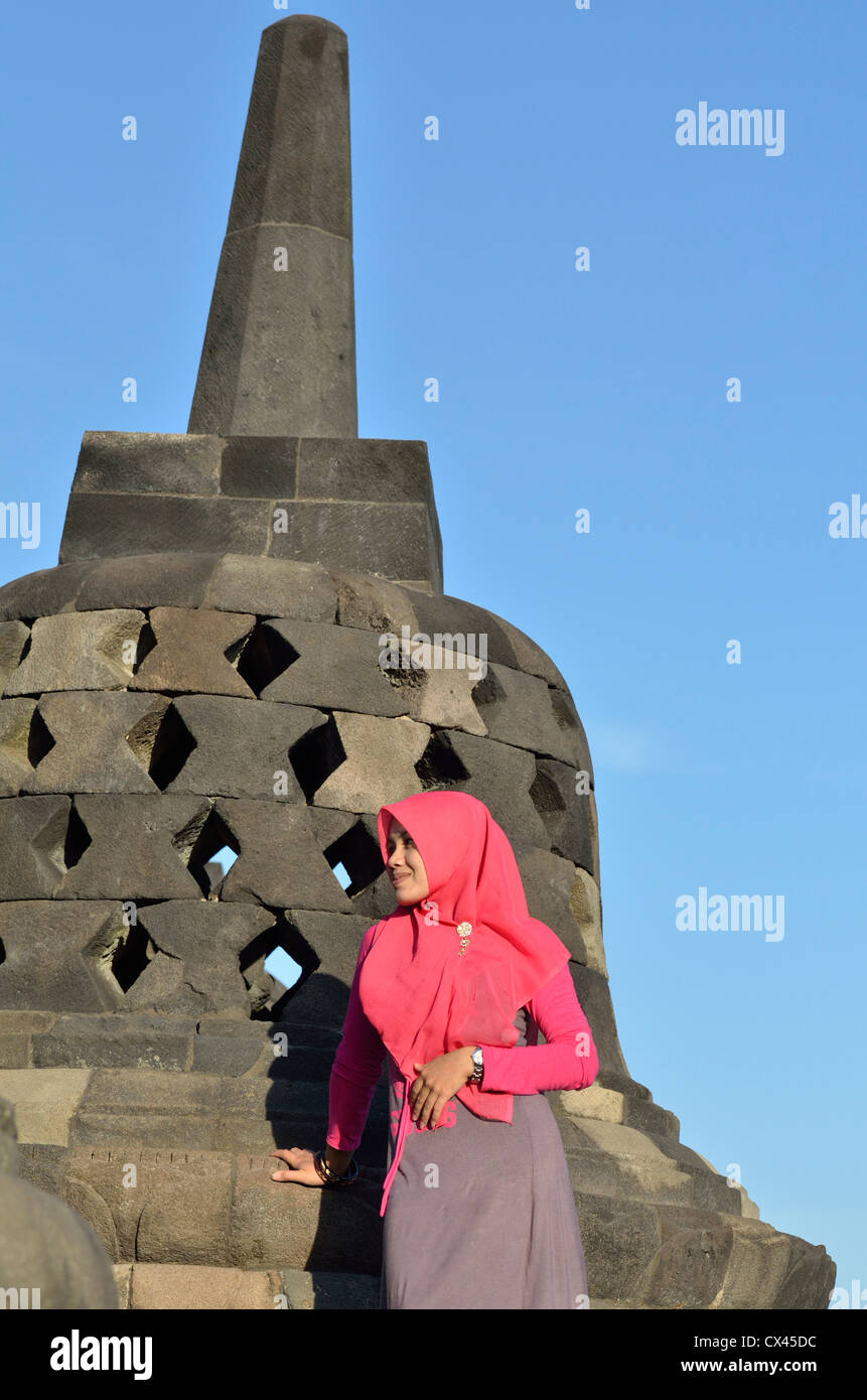 A brightly veiled indonesian woman stands beside one of the stupa at Borobudur; Central Java, Indonesia. Stock Photo