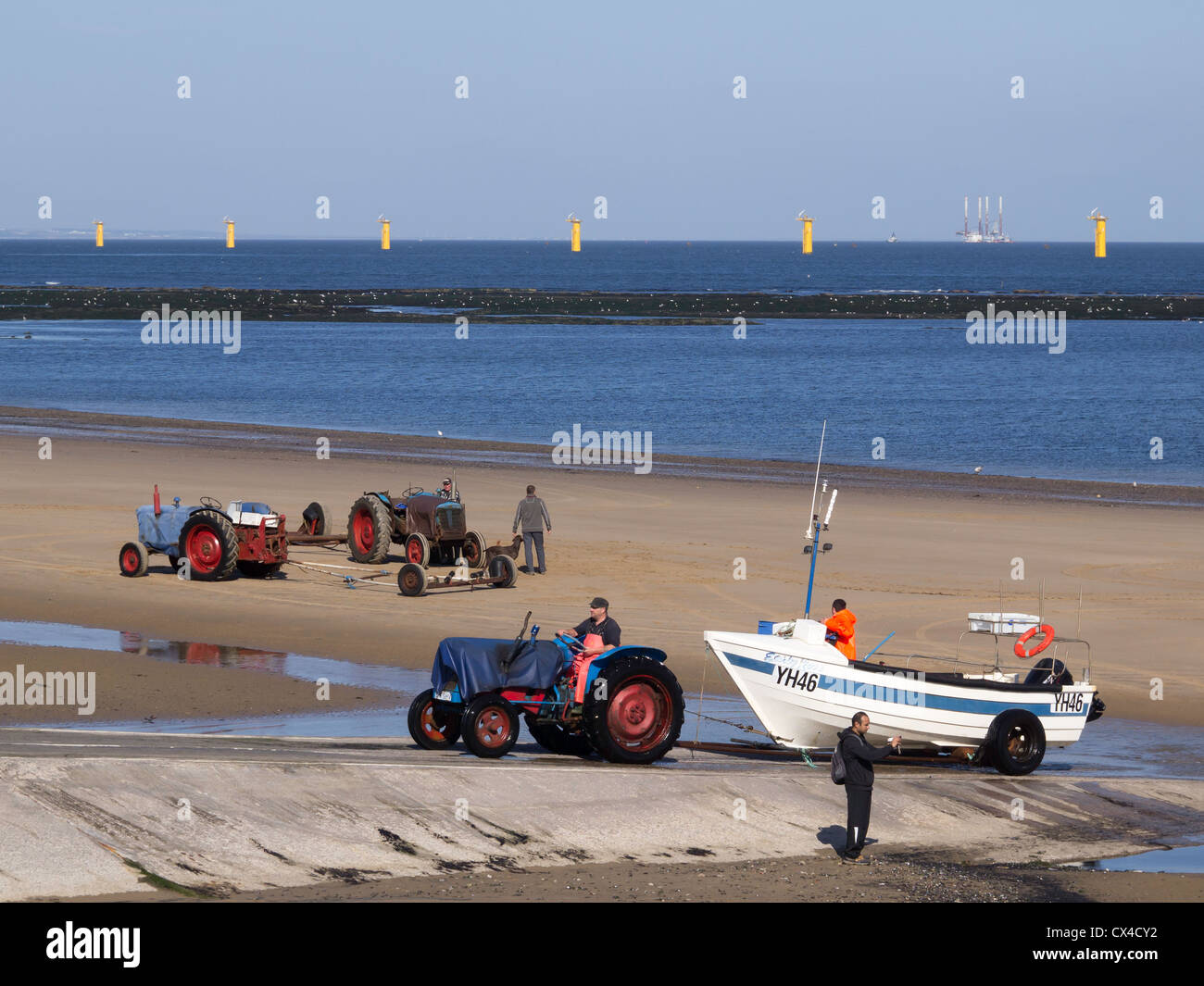 Inshore fishermen bringing a boat ashore at Redcar Cleveland with bright yellow bases for the new wind turbines 2012 Stock Photo
