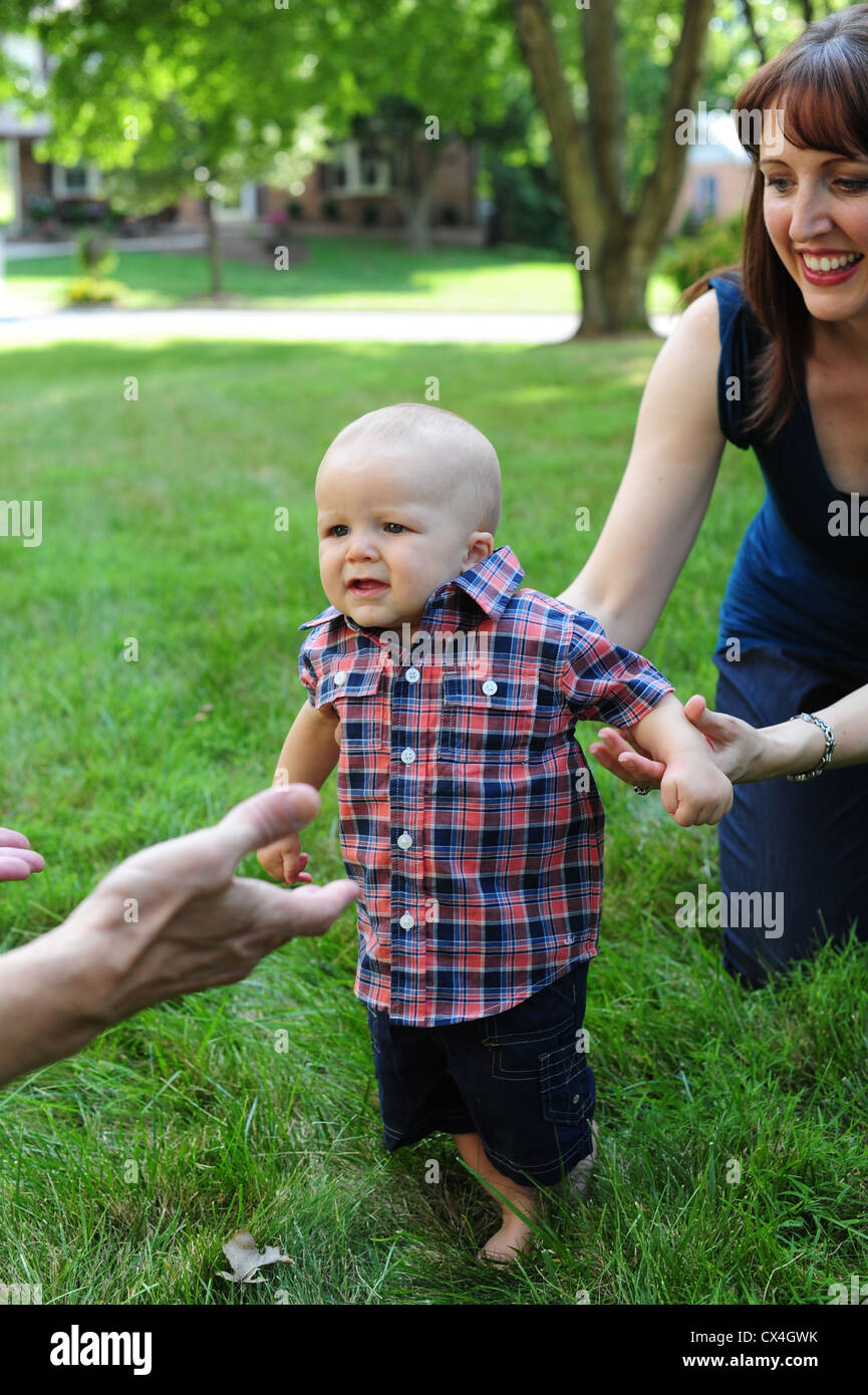 White Caucasian Mother Father with baby son taking his first steps learning to walk outdoors Stock Photo