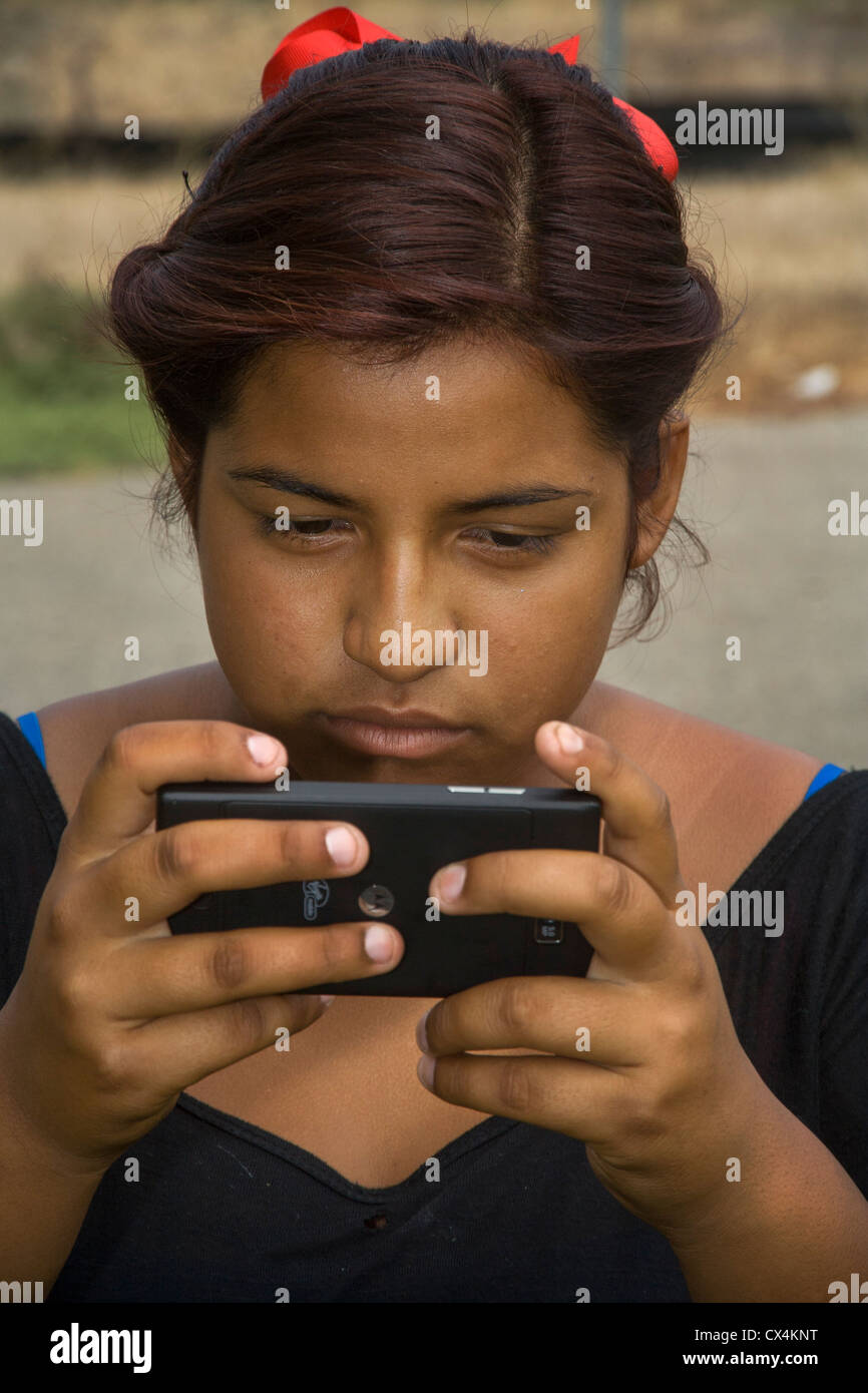 An upset Hispanic girl reads a bullying message on her Smart Phone. Stock Photo