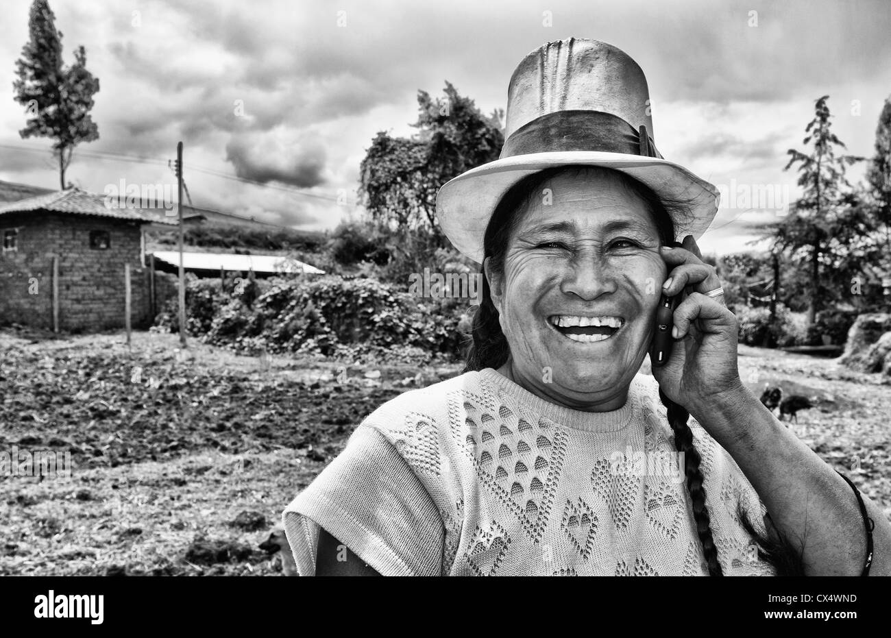 Wonderful farming woman on farm with cell phone in traditional dress and smiling happy workers in Chinchero Peru Stock Photo
