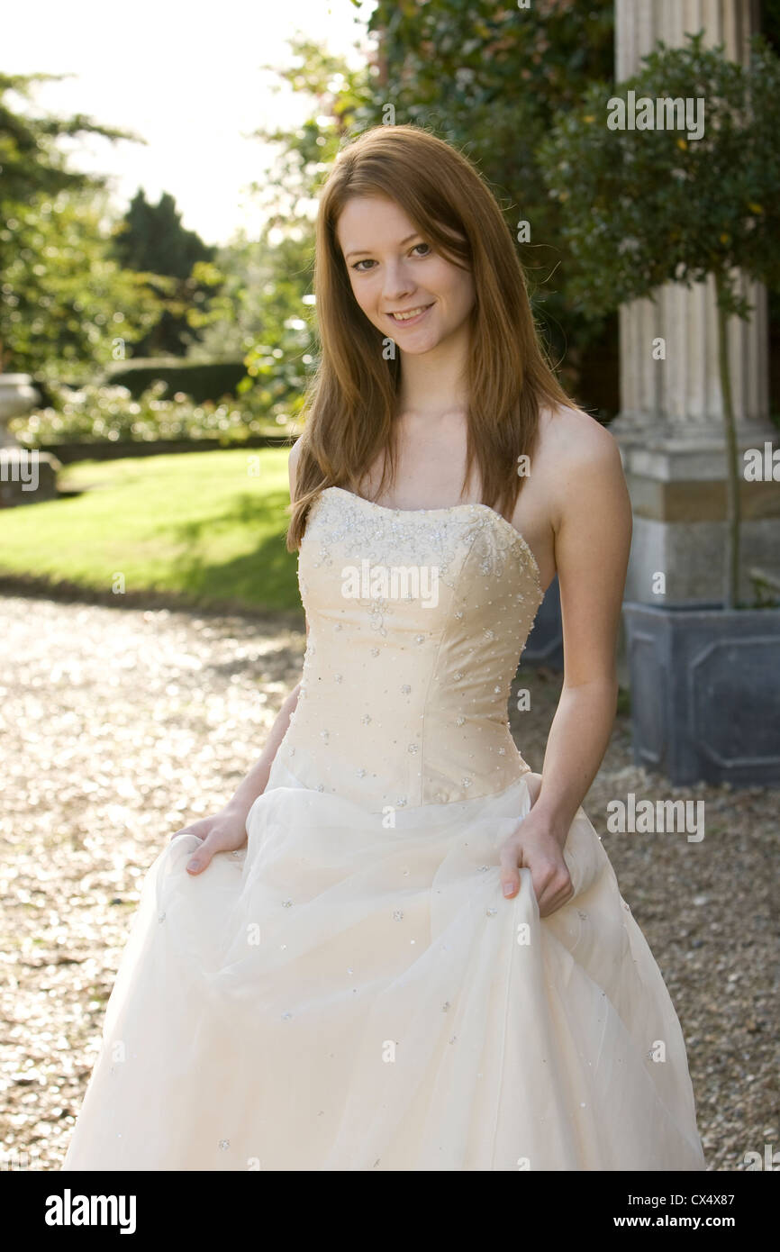 Young woman in cream strapless bridal gown holding skirts in grounds of stately home Stock Photo