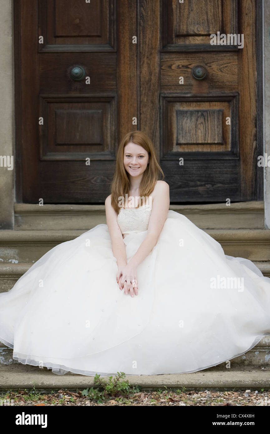 Young woman in bridal dress with full skirt poses sitting on steps in front  of large traditional wooden doors Stock Photo - Alamy