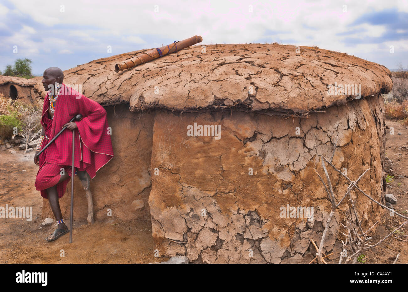 Kenya Africa Amboseli Maasai tribe village Masai man in red costume dress and beads in front of mud home in remote area #1 Stock Photo