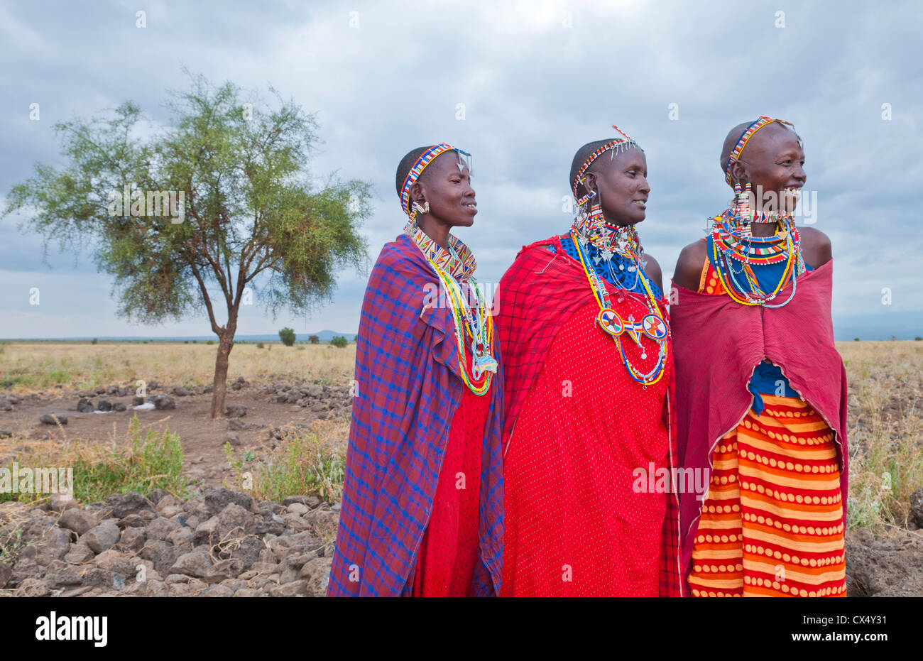 Kenya Africa Amboseli Maasai tribe village Masai women in red costume dress and beads and tree in remote area #1 Stock Photo