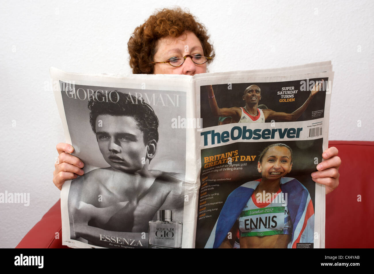 Woman reading a copy of The Observer newspaper with the headline 'Britain's greatest day' Stock Photo