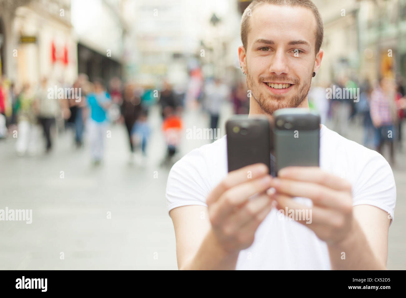 Man holding in hands two mobile phone, blurred city street and people ...