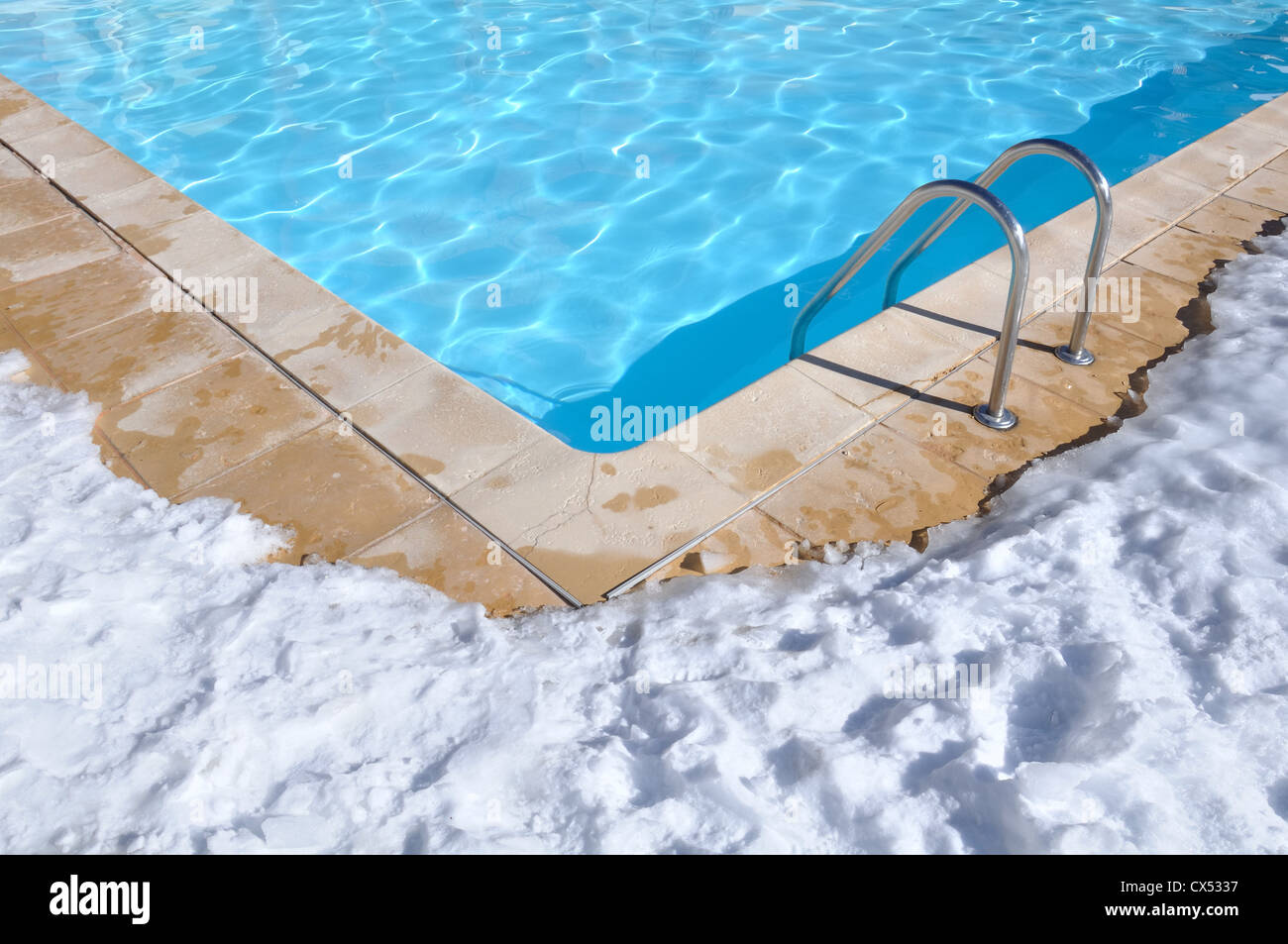 blue water of a swimming pool with outdoor terrace covered in snow Stock Photo