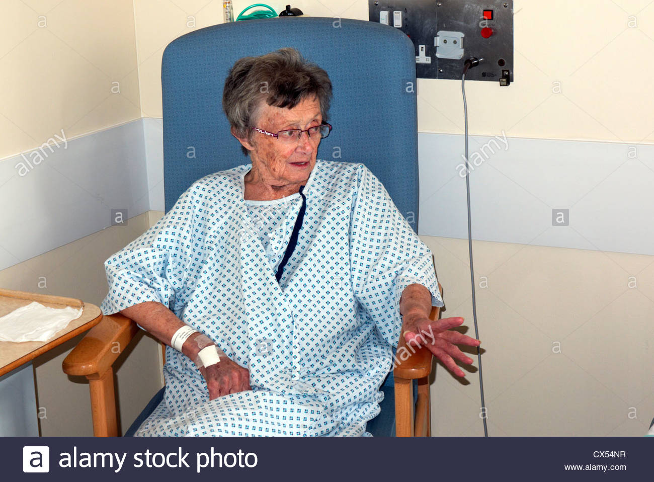 elderly woman patient 90s sitting in a chair at her bedside in a Stock