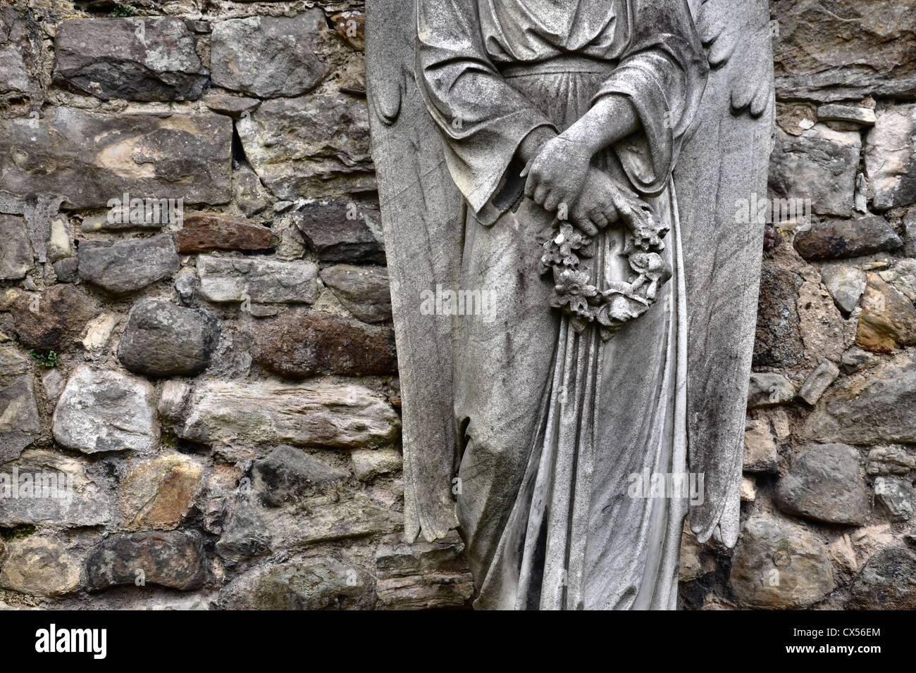 Partial view of an angel holding a wreath standing against the stone wall of the Dean Cemetery in Edinburgh, Scotland, UK. Stock Photo