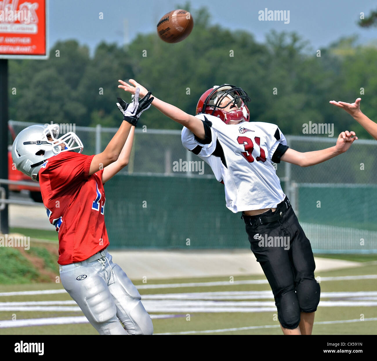 At the end zone a young boy reaching to catch the pass as a blocker tries to intercept. Stock Photo