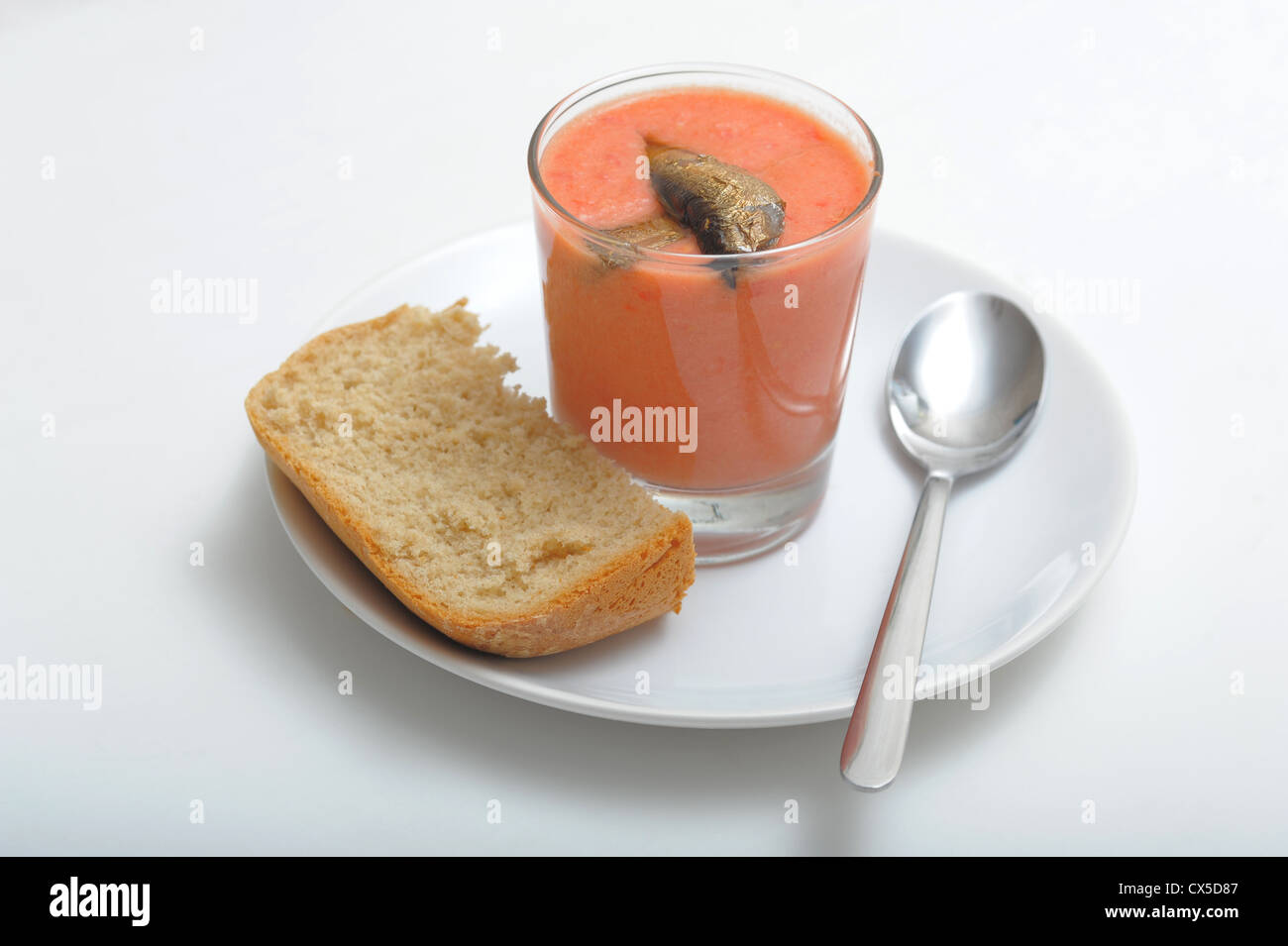 Served homemade gazpacho with sprats in the cup with spoon and bread on the white plate Stock Photo