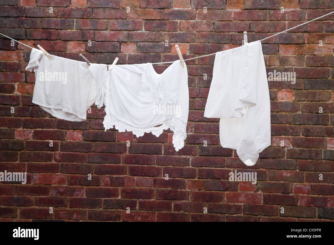 A re-creation of a Victorian washing line within a brick walled yard - with white garments hanging on a rope and dolly pegs. UK. Stock Photo