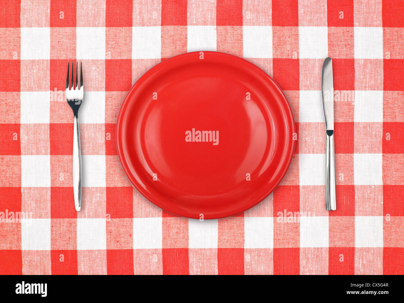 Knife, red plate and fork on checked tablecloth Stock Photo