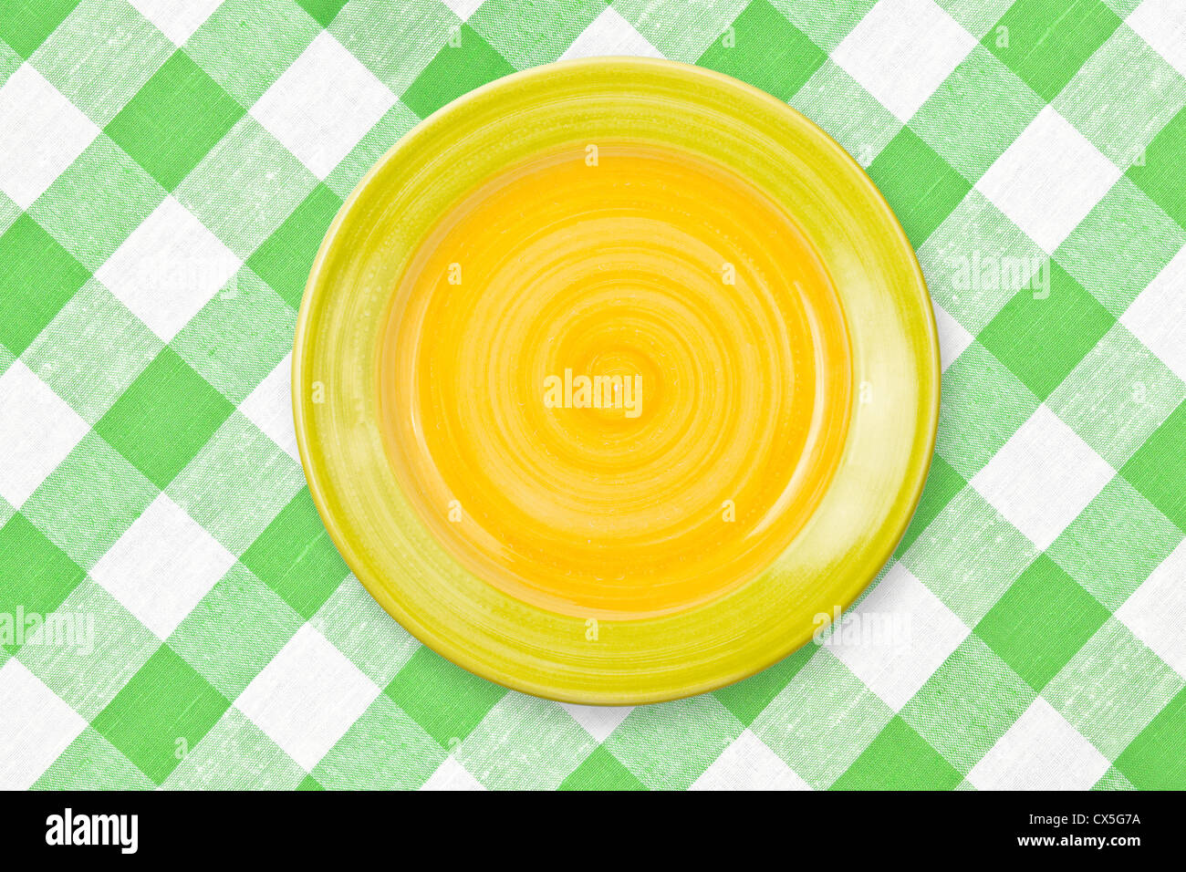Round yellow plate on checked tablecloth Stock Photo