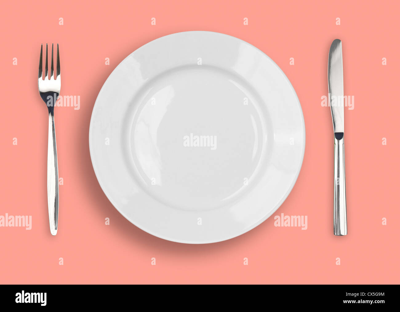 Knife, white plate and fork on rose background Stock Photo