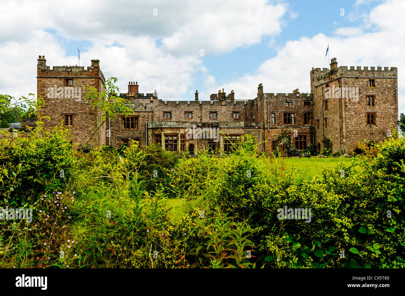 The historic medieval facade of Muncaster Castle with its two crenelated towers set in the green woodland of the Lake District Stock Photo