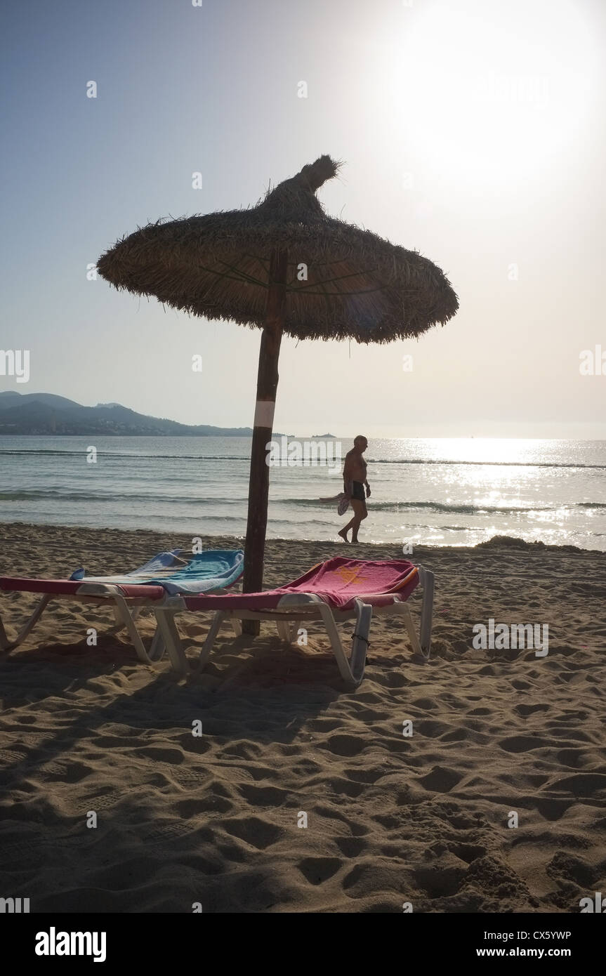 A lone walker on the beach next to a sunbed as the sun rises on a summers day Stock Photo