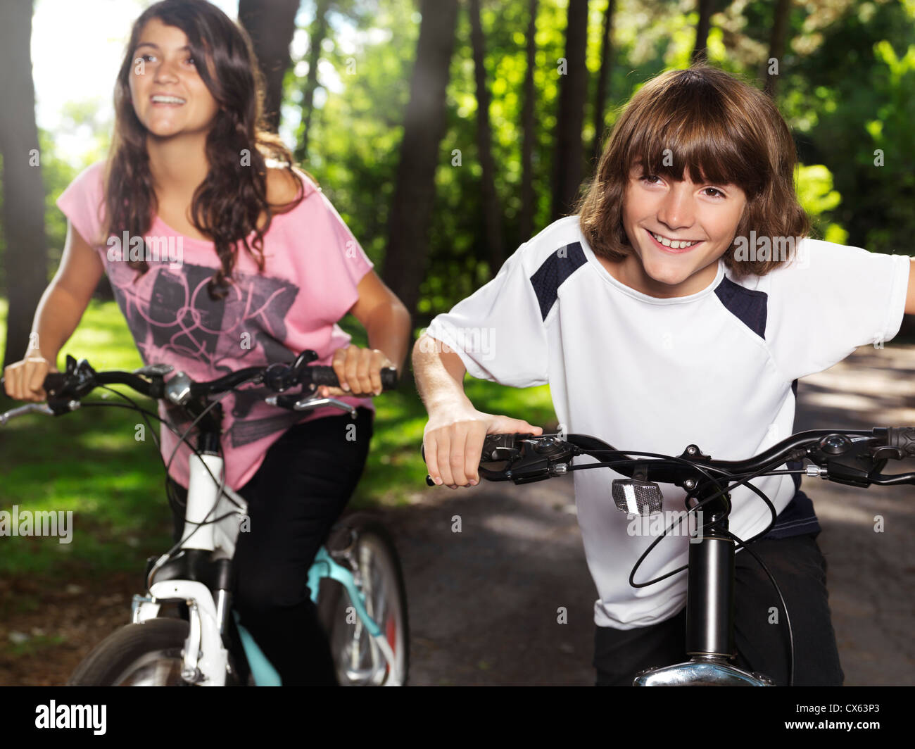 Two happy smiling children riding bicycles in a park, brother and sister, 10 and 13. Active outdoor lifestyle. Stock Photo