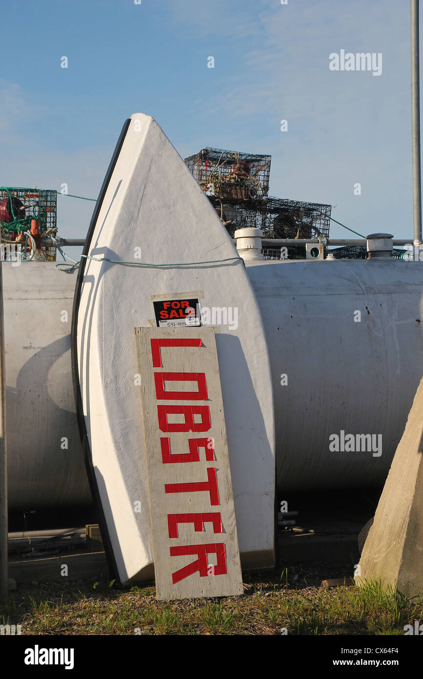'Lobster' sign and rowboat with a for-sale sign propped against a fuel tank, lobster traps in the background. Stock Photo