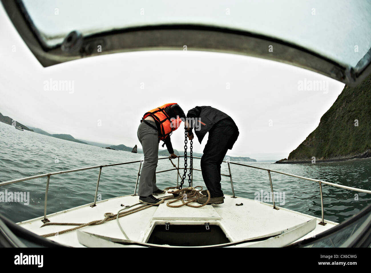 Two people engaged in lowering an anchor off the bow of a boat, Avacha Bay, Russia Stock Photo