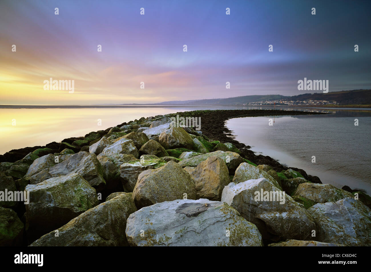 Stone sea defenses at Llanelli beach with Pwll in the distance taken with a long exposure. Stock Photo