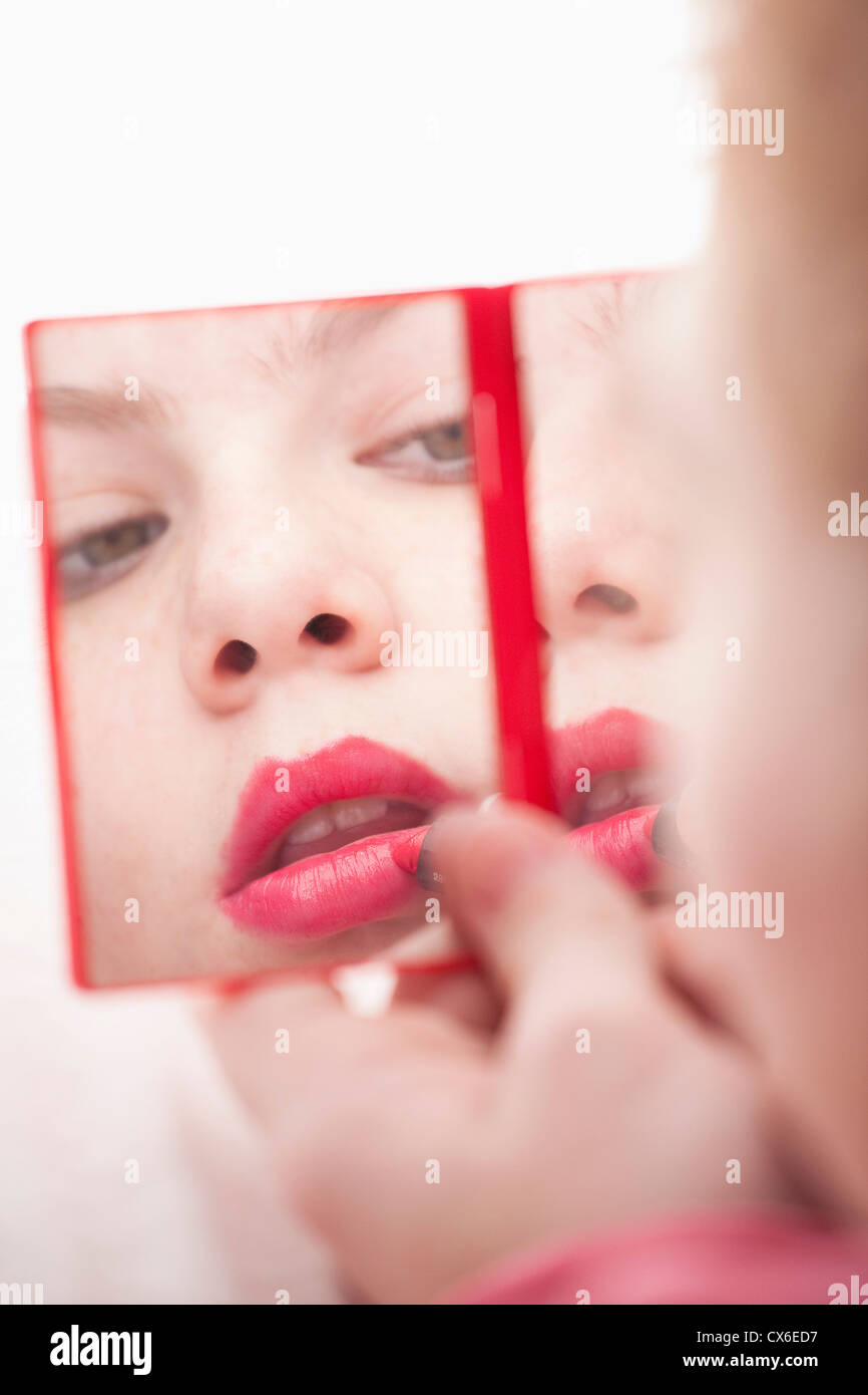 Girl holding hand mirror and applying lipstick Stock Photo
